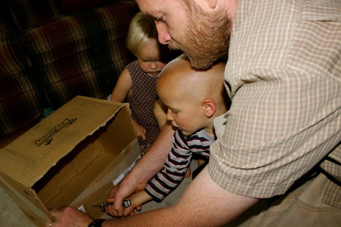 A father helping his son cut a cardboard box.
