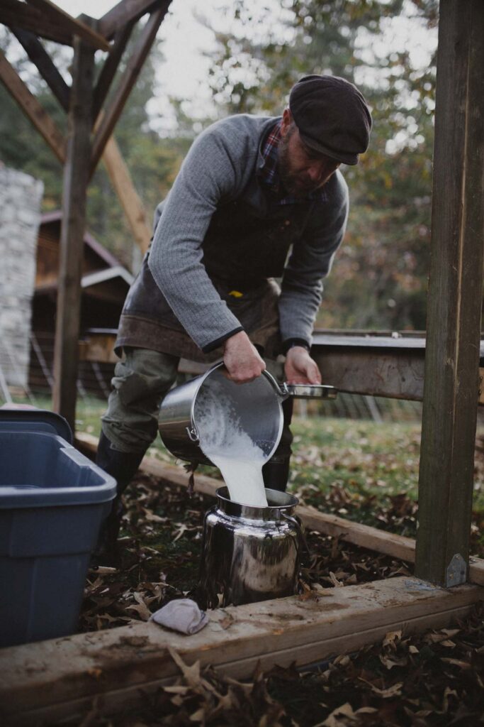 A man pouring fresh milk into a stainless steel container.