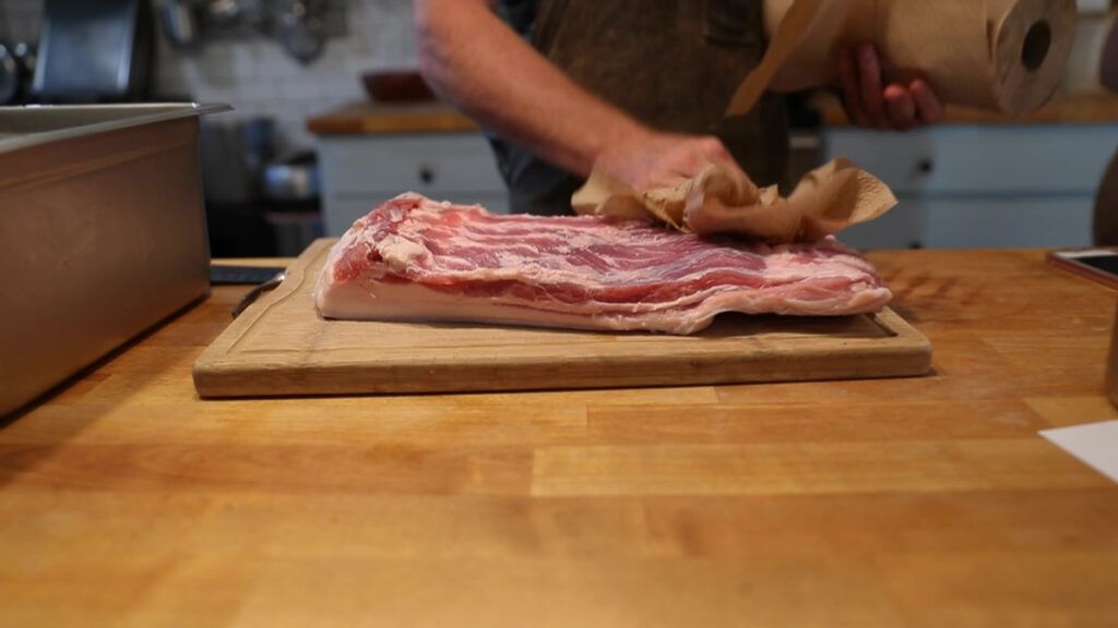A man drying off a slab of pork belly with paper towels.