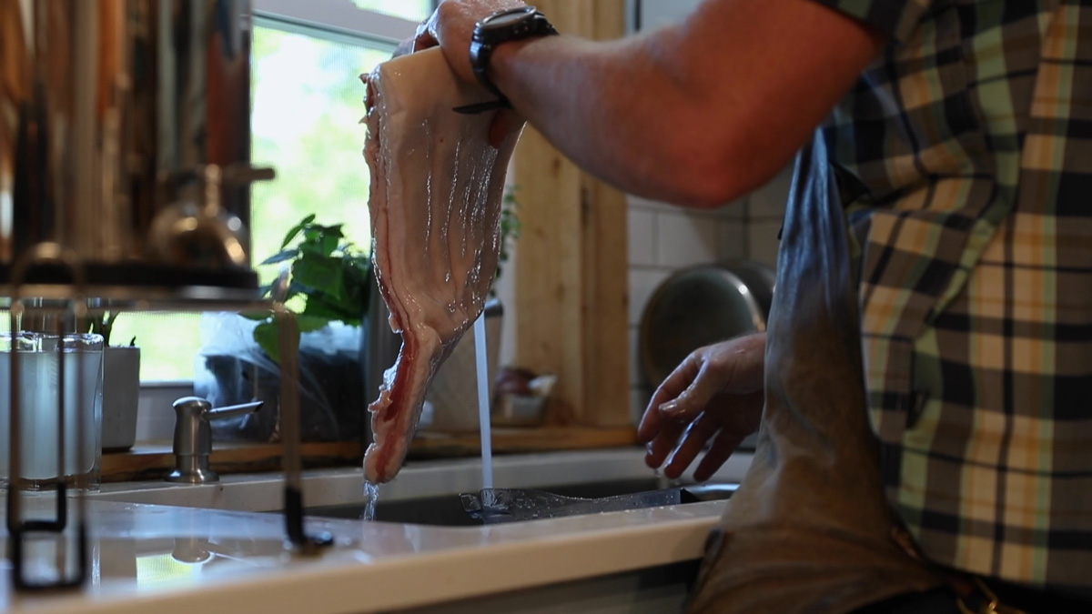 A man rinsing a slab of pork belly under running water.