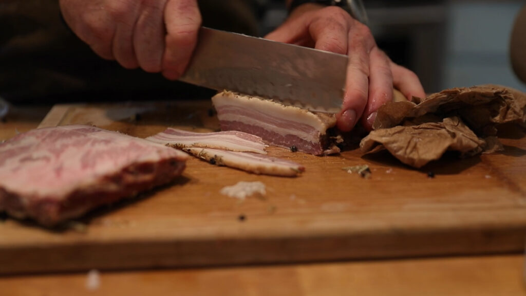 Cured slab of bacon getting cut into strips.