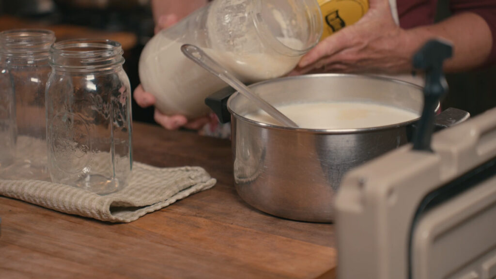 A woman pouring yogurt culture into a pot of milk.