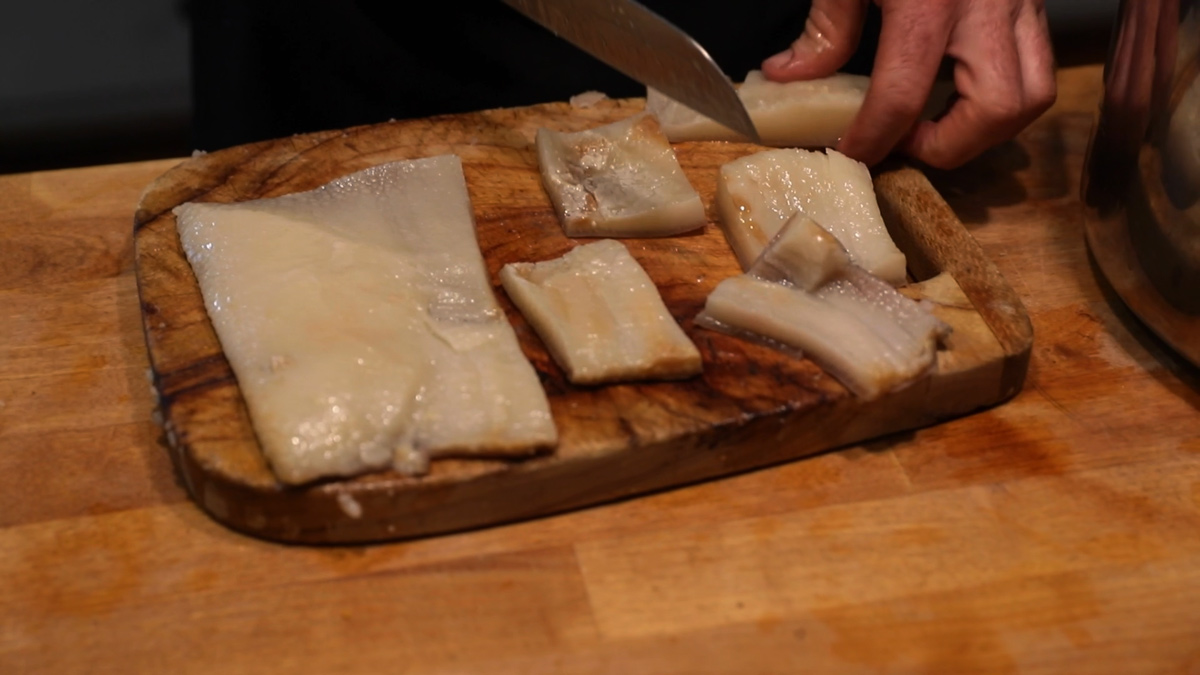 A man cutting strips of pork skin into "chip" sized pieces.