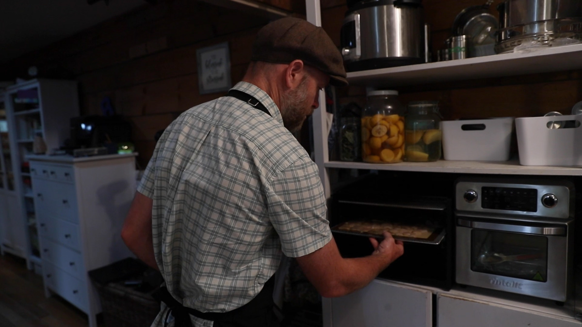 A man sliding a tray of pork skins into the dehydrator.