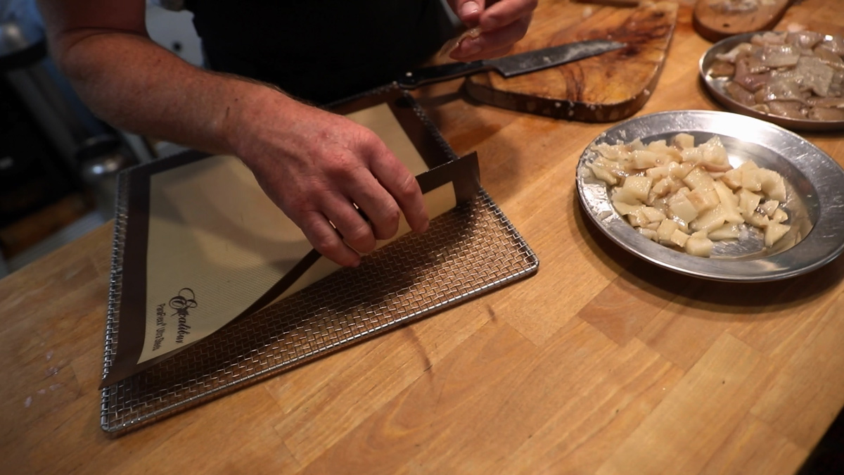 A man laying a silpat mat on a dehydrator tray.