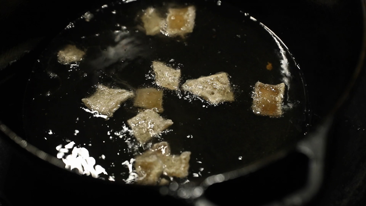 Pork rinds frying in a cast iron pan of oil.