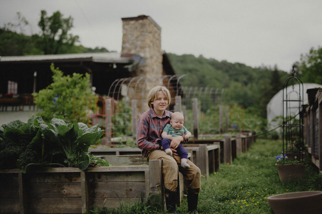 A boy holding a baby sitting on a raised garden bed.